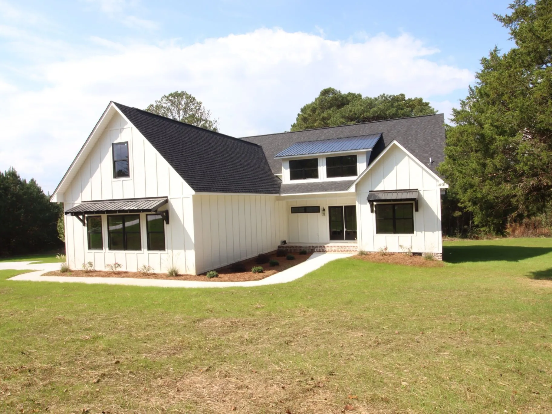 Completed JC T1 home exterior with white board-and-batten siding, dark gables, and a broad lawn