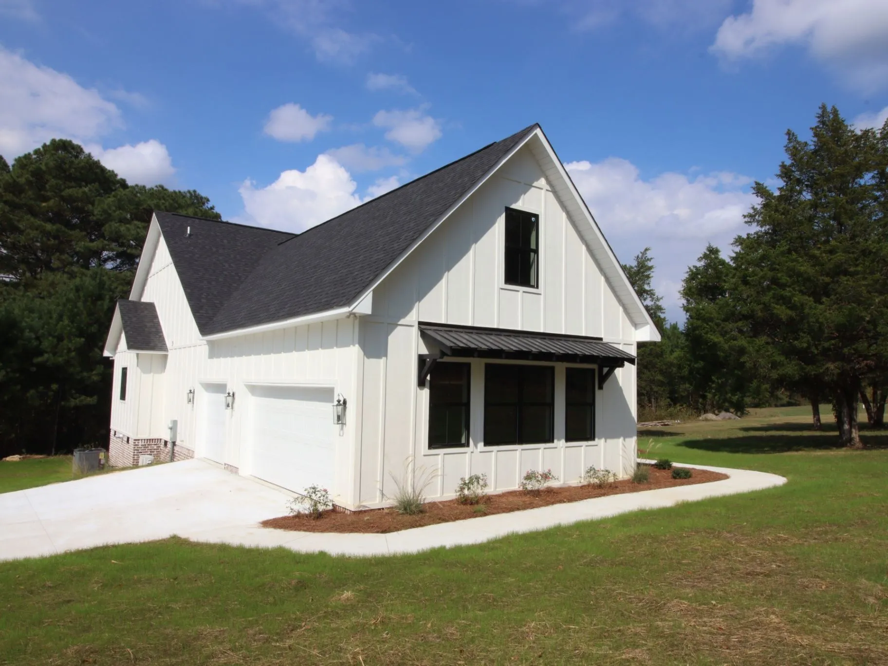 Completed JC T1 home exterior showing the garage, white siding, dark roof, and landscaped approach