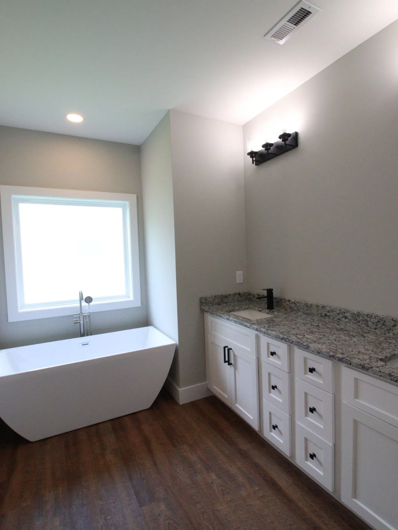 Completed JP2 New Construction bathroom with a freestanding tub, white vanity, and bright window