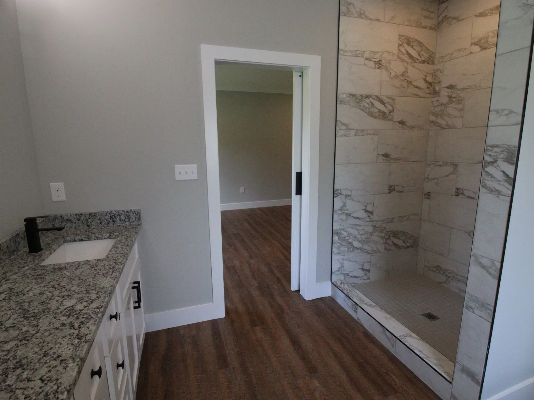 Completed JP2 New Construction bathroom with a tiled shower, white vanity, and wood-look floor