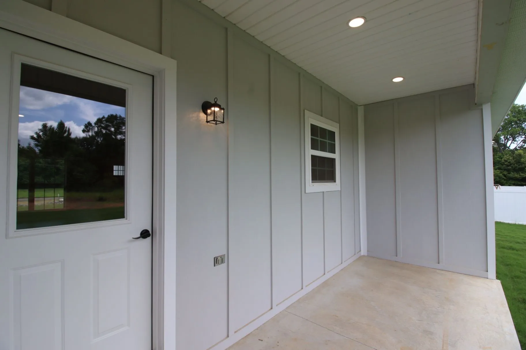 Completed JP2 New Construction covered entry with gray siding, a porch light, and landscaped approach